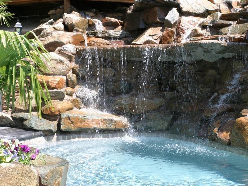 Water cascades over rocks into a pool; lush vegetation surrounds the water feature.