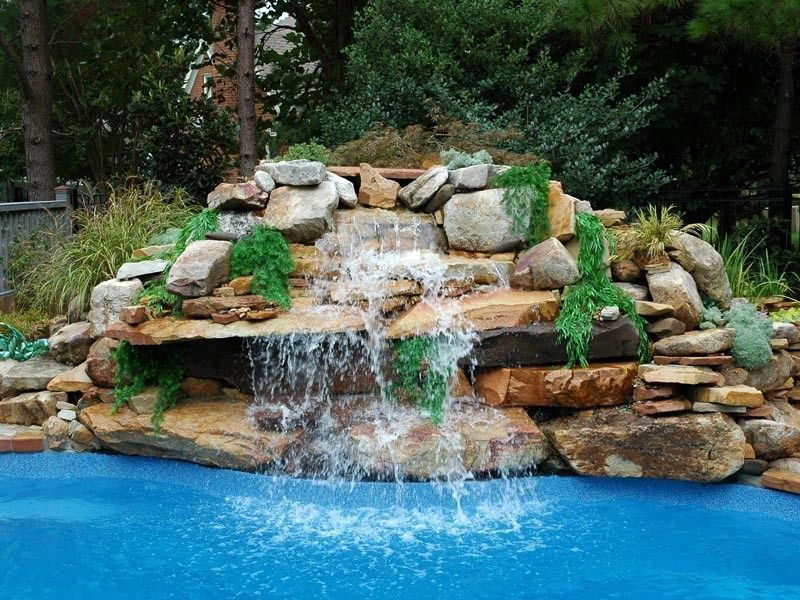 Waterfall cascading over rocks into a blue pool, surrounded by greenery.