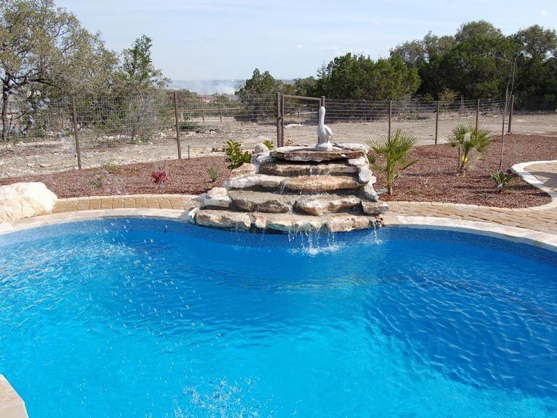 Pool with water feature, blue water, stone tiers, and a statue, surrounded by landscaping.