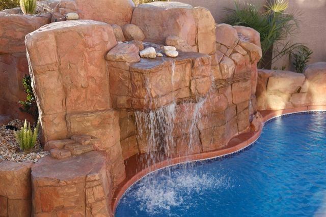 Pool with a red rock waterfall feature and clear blue water.