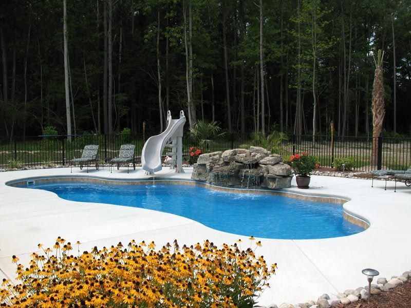 Swimming pool with a water slide, rock waterfall, and trees in the background.