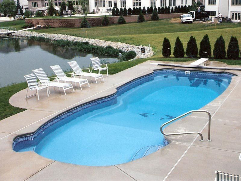 Swimming pool with blue water, concrete surround, and white lounge chairs beside a pond.