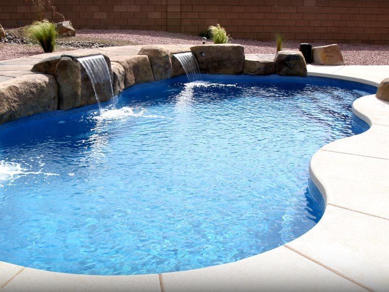 Swimming pool with waterfalls and stone accents; blue water, light-colored patio.