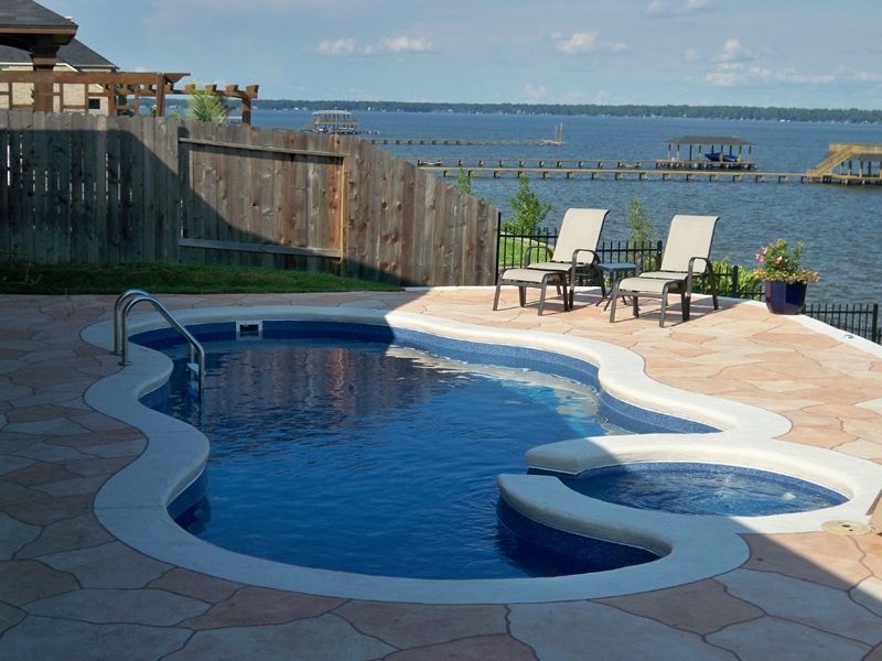 Swimming pool with water feature, overlooking a lake, with two chairs.