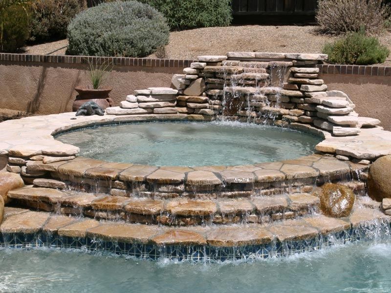 Water cascades down a stone waterfall into a spa, adjacent to a swimming pool.
