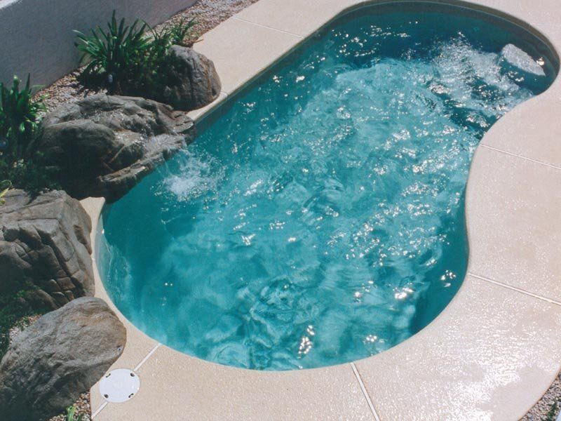 Small, teal-colored jacuzzi with bubbling water, surrounded by beige concrete and rocks.