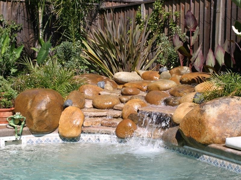 Backyard pool with a rock waterfall feature and lush greenery.