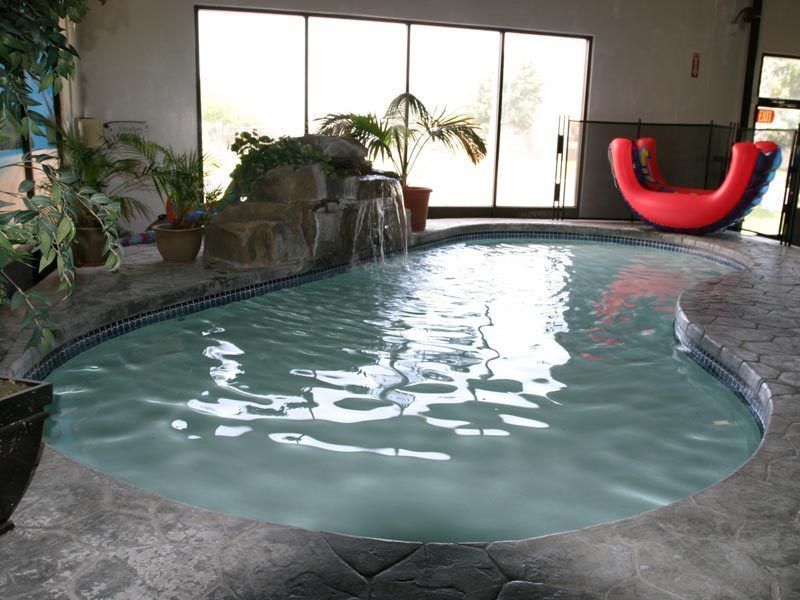 Indoor pool with waterfall feature, potted plants, and red inflatable toy.