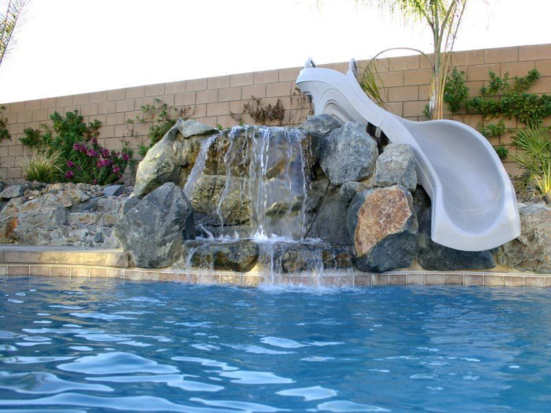 A pool with a waterfall feature, rock formation, and a slide.