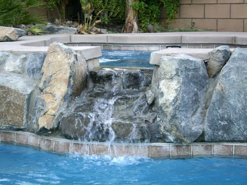 Water cascades over rocks into a blue swimming pool.