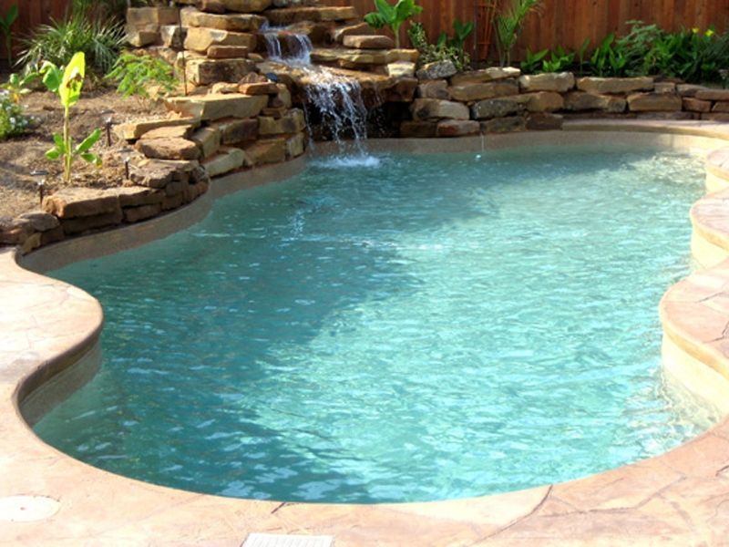Swimming pool with waterfall feature; surrounded by stone landscaping and plants.
