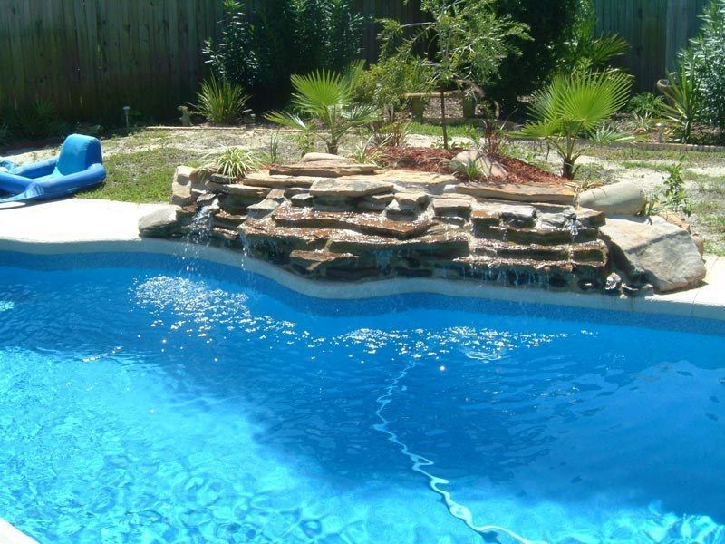 Blue swimming pool with a rocky waterfall feature, palms, and a blue raft.