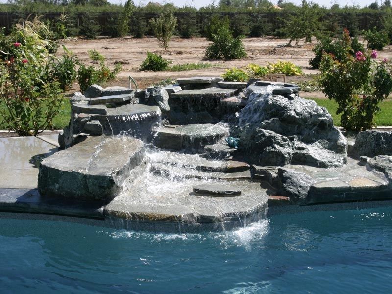 Water cascades down a multi-level stone waterfall into a swimming pool.