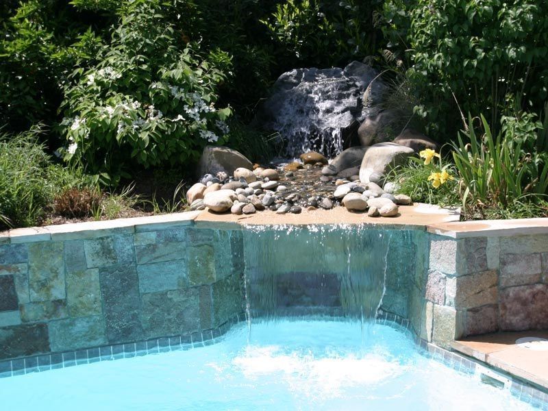 Waterfall cascades into a swimming pool; rocks, plants, and blue water.