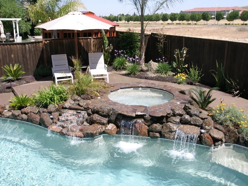 Pool with hot tub, waterfall feature, and two lounge chairs in a backyard setting.