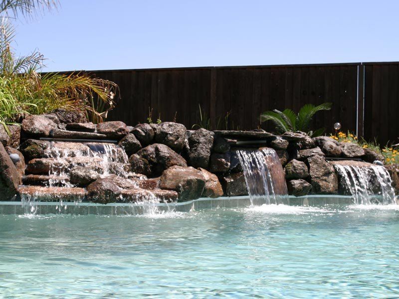 Pool with three cascading waterfalls flowing from a rock formation into clear blue water.