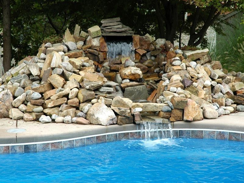 Rock waterfall feature cascading into a blue swimming pool.