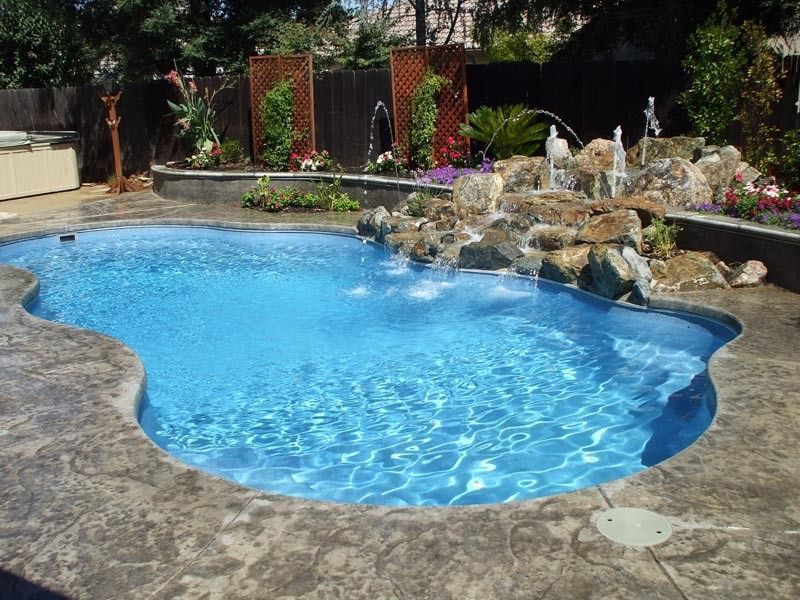 Swimming pool with a rock waterfall feature and surrounding landscaping.