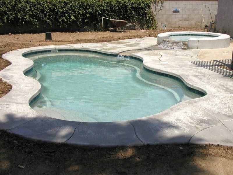 Swimming pool with a connected hot tub, concrete coping, and a grassy backyard.