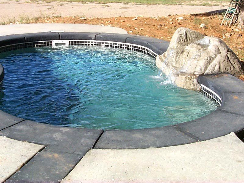 Circular hot tub with a small waterfall feature. Dark border, light blue water.