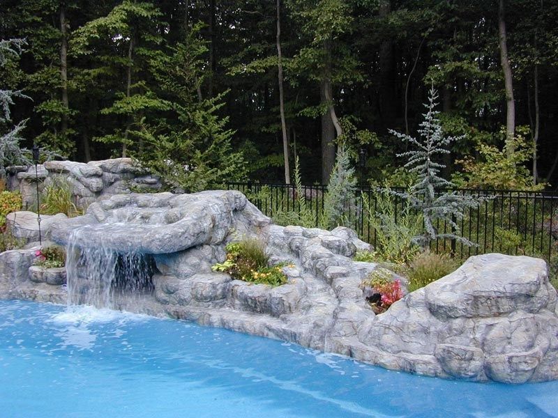 Waterfall feature cascading into a swimming pool with a forest backdrop.