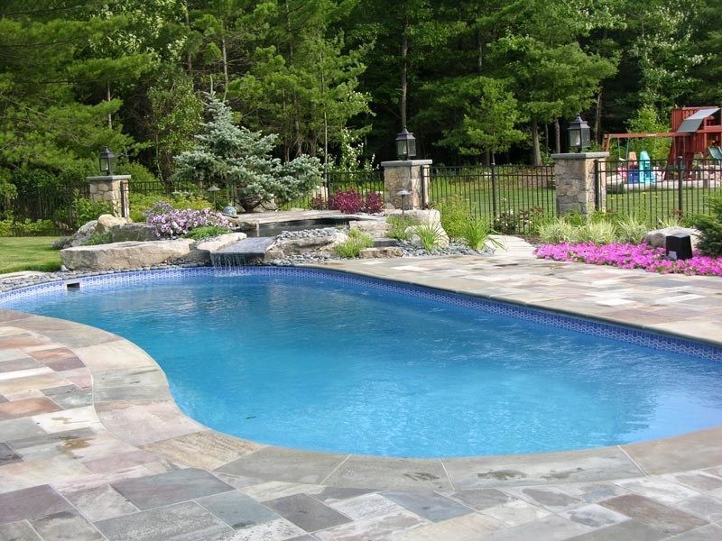 Swimming pool with a stone patio, waterfall, and surrounding landscaping.