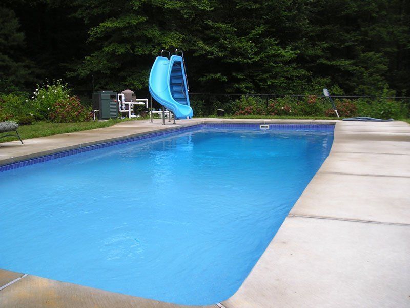 Blue swimming pool with a water slide in a backyard setting.