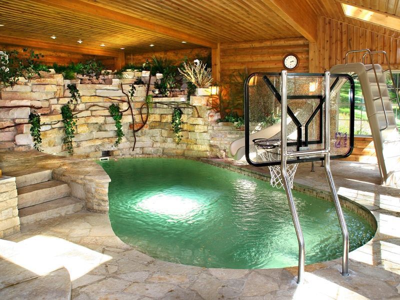 Indoor pool with stone steps and waterfall feature, basketball hoop, and slide.