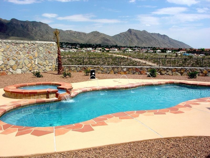 Swimming pool with attached spa, stone wall, and desert mountain backdrop.