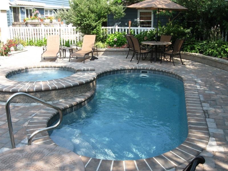 Small backyard pool with attached hot tub, lounge chairs, and patio table.