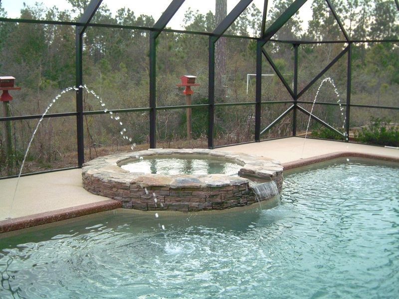 Pool with a built-in spa; water jets arc into the pool. Screened enclosure with natural background.