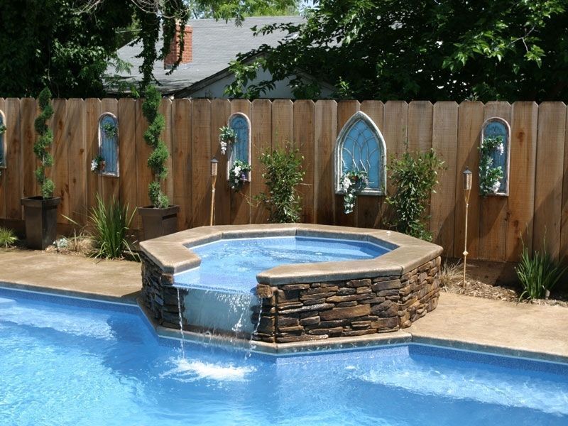 Swimming pool with a stone hot tub and a wooden fence with decorative arches.