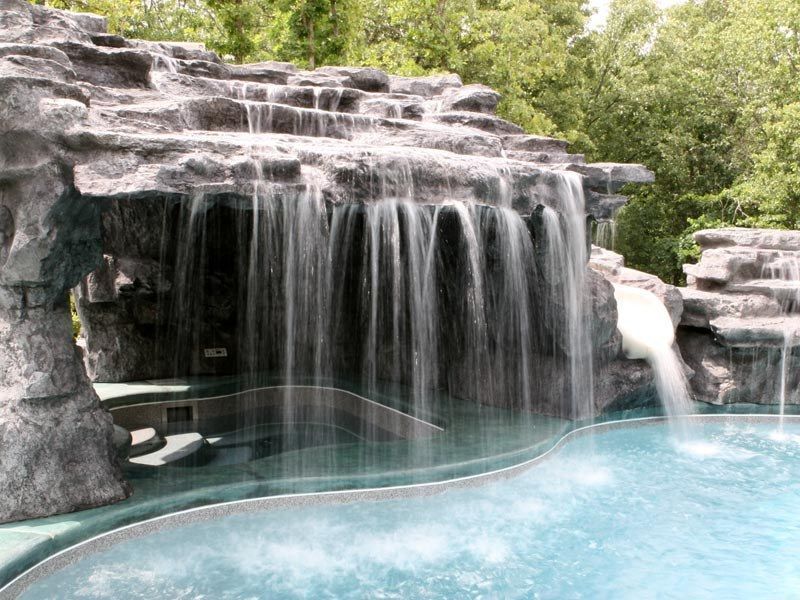 Waterfall feature cascading into a pool with stone formations and lush trees in the background.