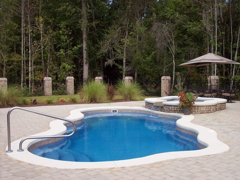 Swimming pool with a connected hot tub, surrounded by a stone patio and landscaping.