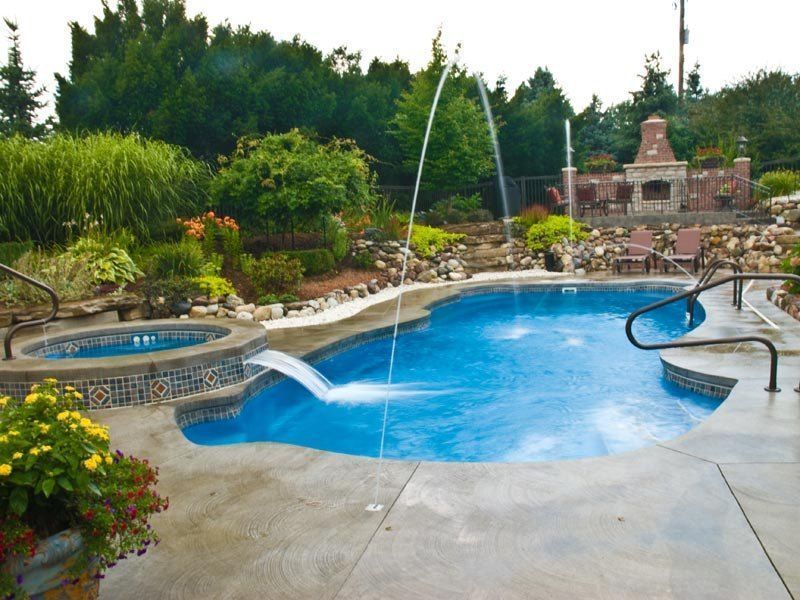 Pool with water features, surrounded by landscaping, hot tub, and outdoor fireplace.