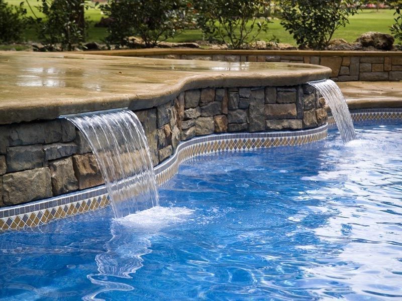 Pool with stone wall featuring two cascading waterfalls. Clear blue water.