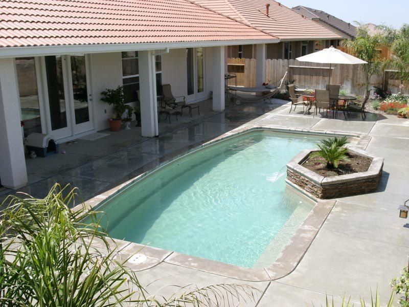 Backyard pool with patio, seating, and a small island with a palm plant.