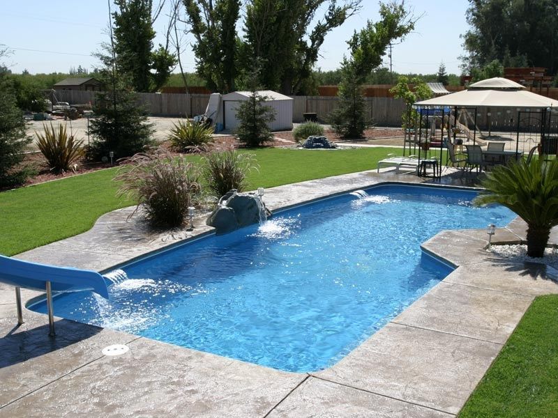 Backyard pool with a slide, waterfall, and patio seating. Blue water and concrete deck.