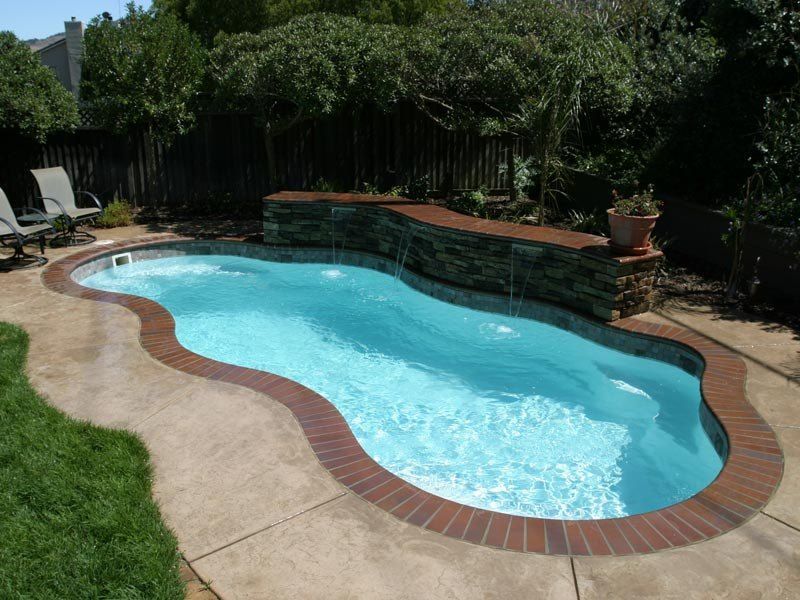 A freeform swimming pool with a brick border and a stone waterfall feature, in a backyard.