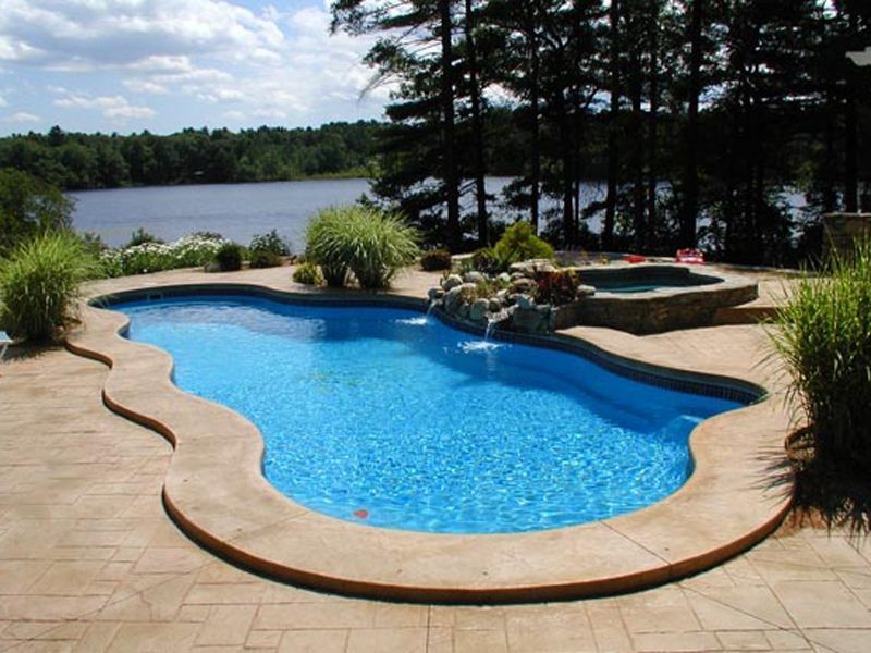 Swimming pool with a lake view; blue water, stone patio, waterfall, and hot tub.