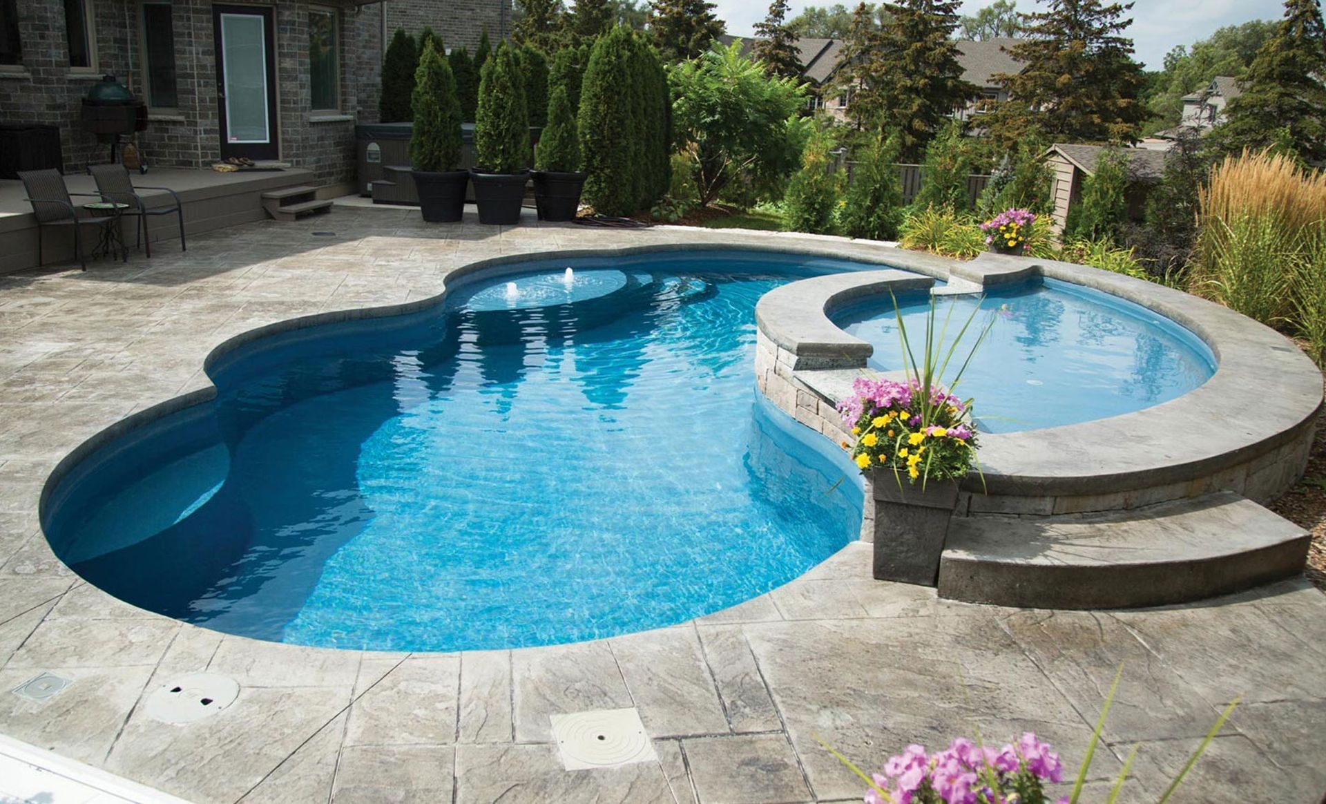 A blue-tiled, kidney-shaped pool with a circular spa, surrounded by stone patio.