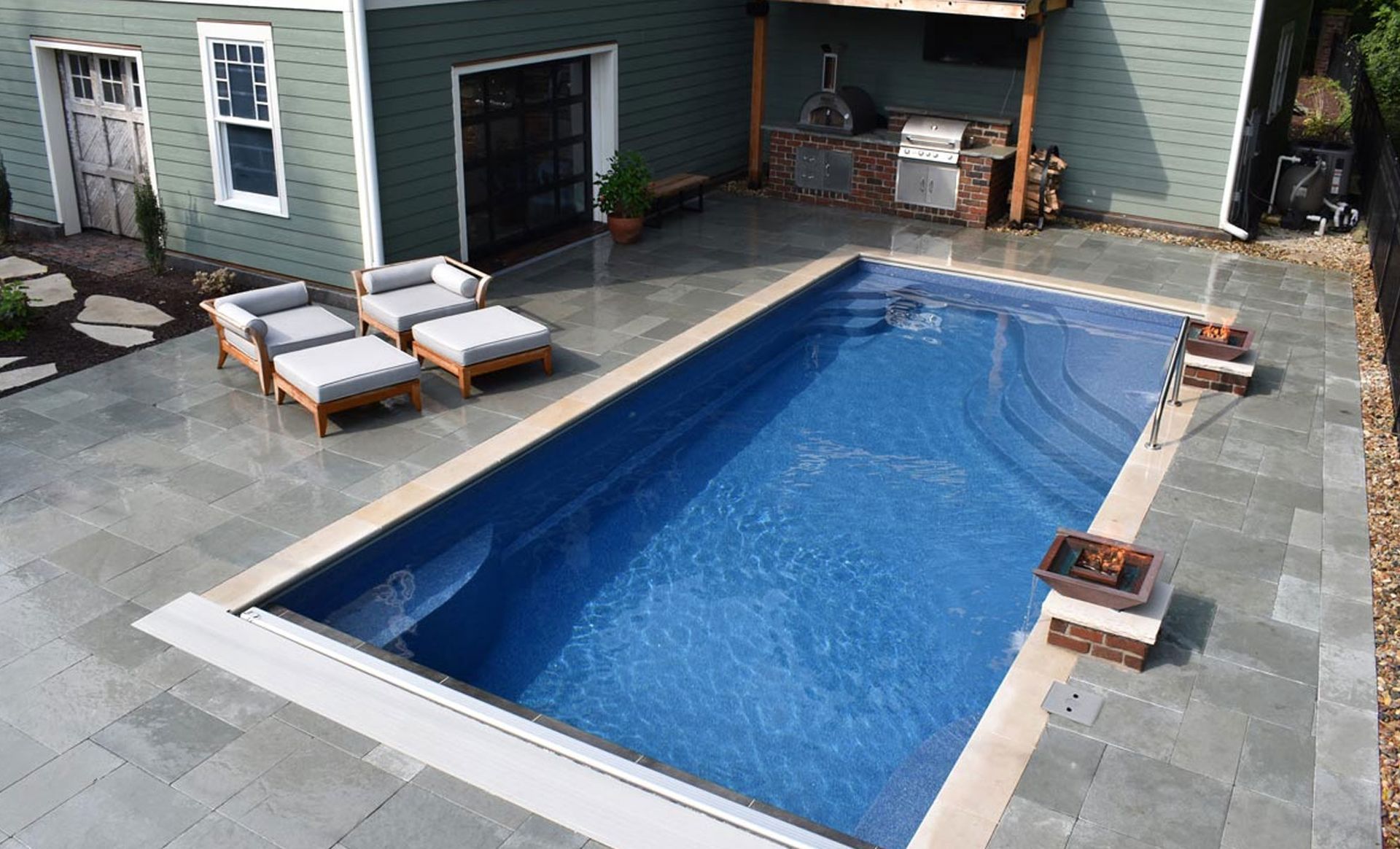 Backyard with a rectangular swimming pool, patio, house, and lounge chairs.