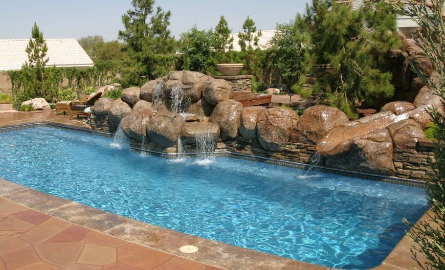 Swimming pool with rock waterfall feature, blue water, and surrounding landscaping.