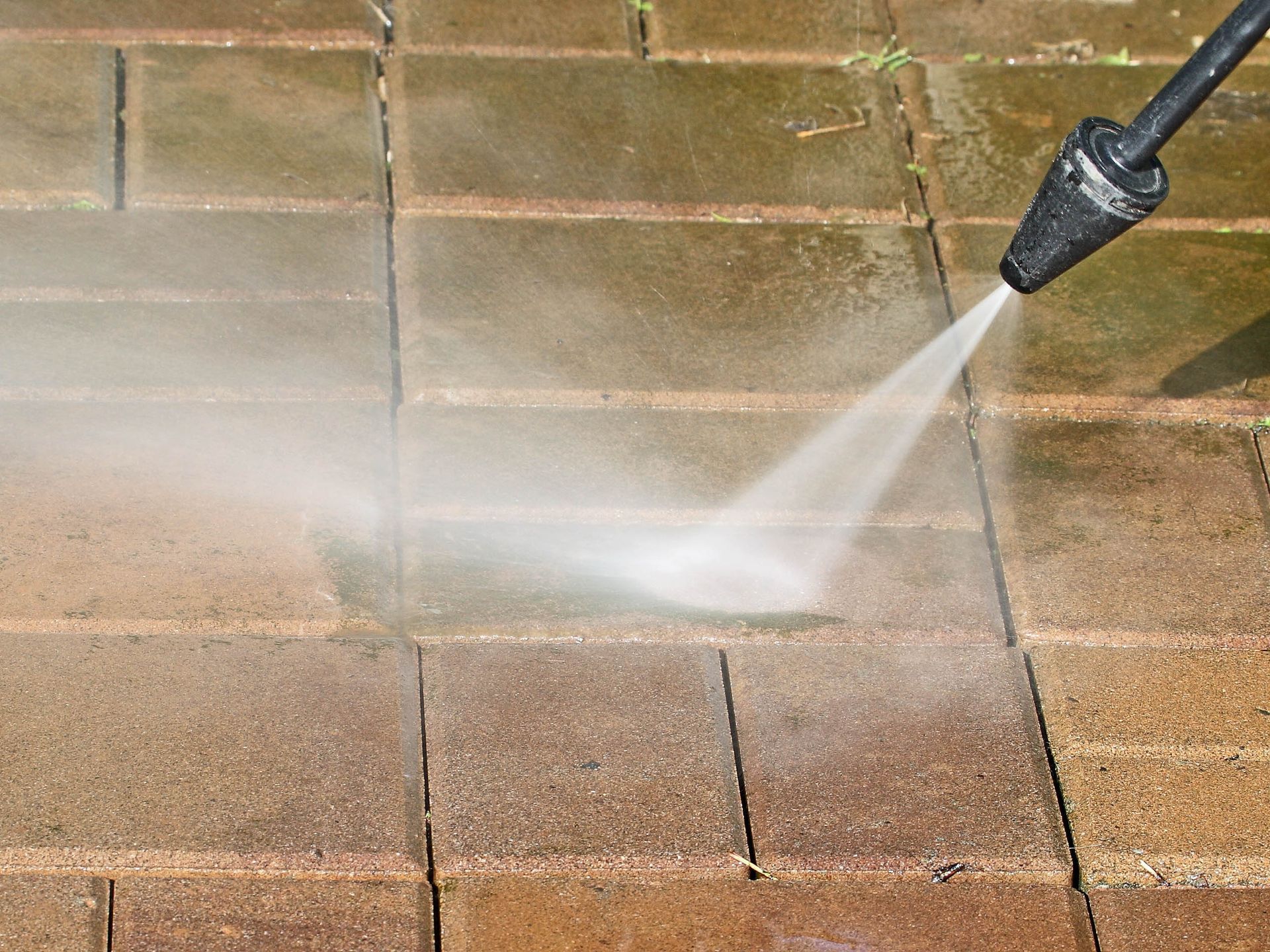 A pressure washer spraying water onto brick pavers, cleaning the surface.