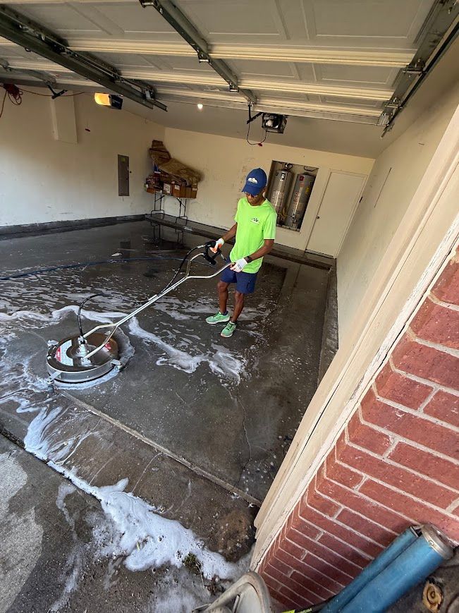 Person cleaning a garage floor with a power washer; white foam visible.