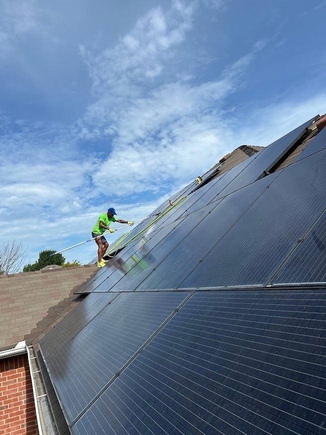 Person on roof cleaning solar panels on a sunny day.