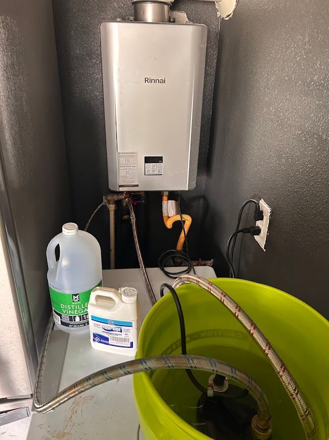 Tankless water heater with cleaning supplies and yellow bucket.