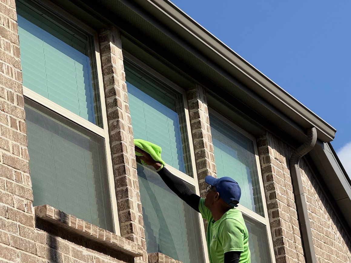 Man in green shirt cleaning a window on a brick building with a blue cap.