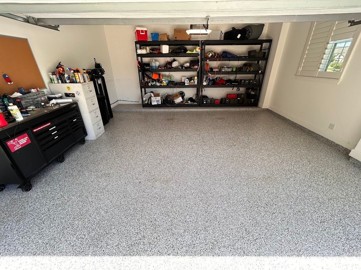 Garage interior with epoxy floor, tool chest, shelving with supplies, and open garage door.