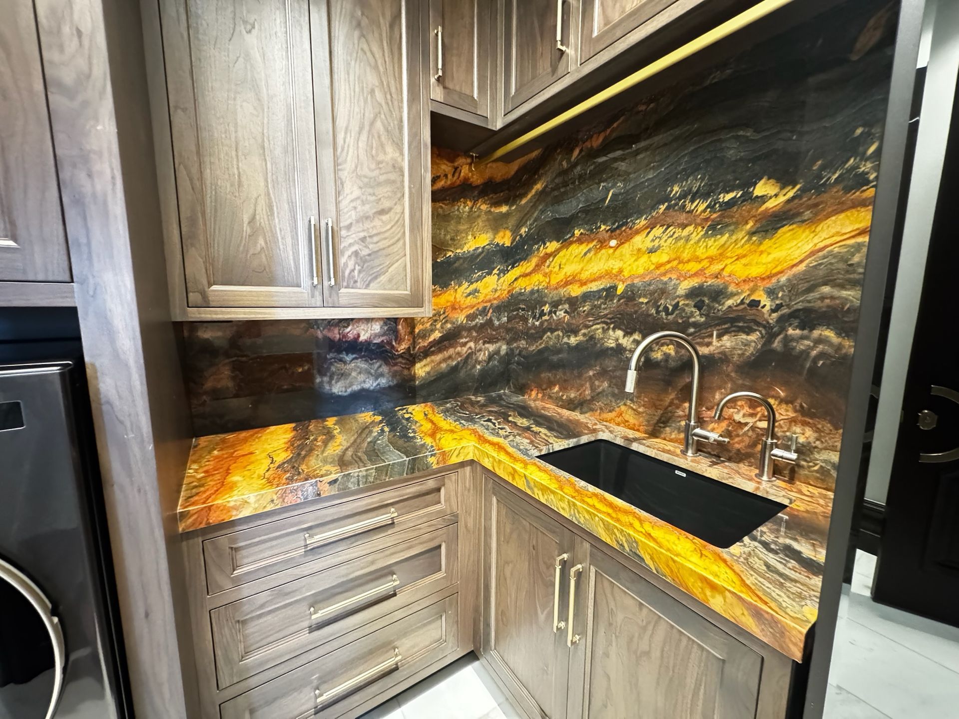 Modern kitchen corner with black-and-gold flame-pattern backsplash, wood cabinets, and a sink